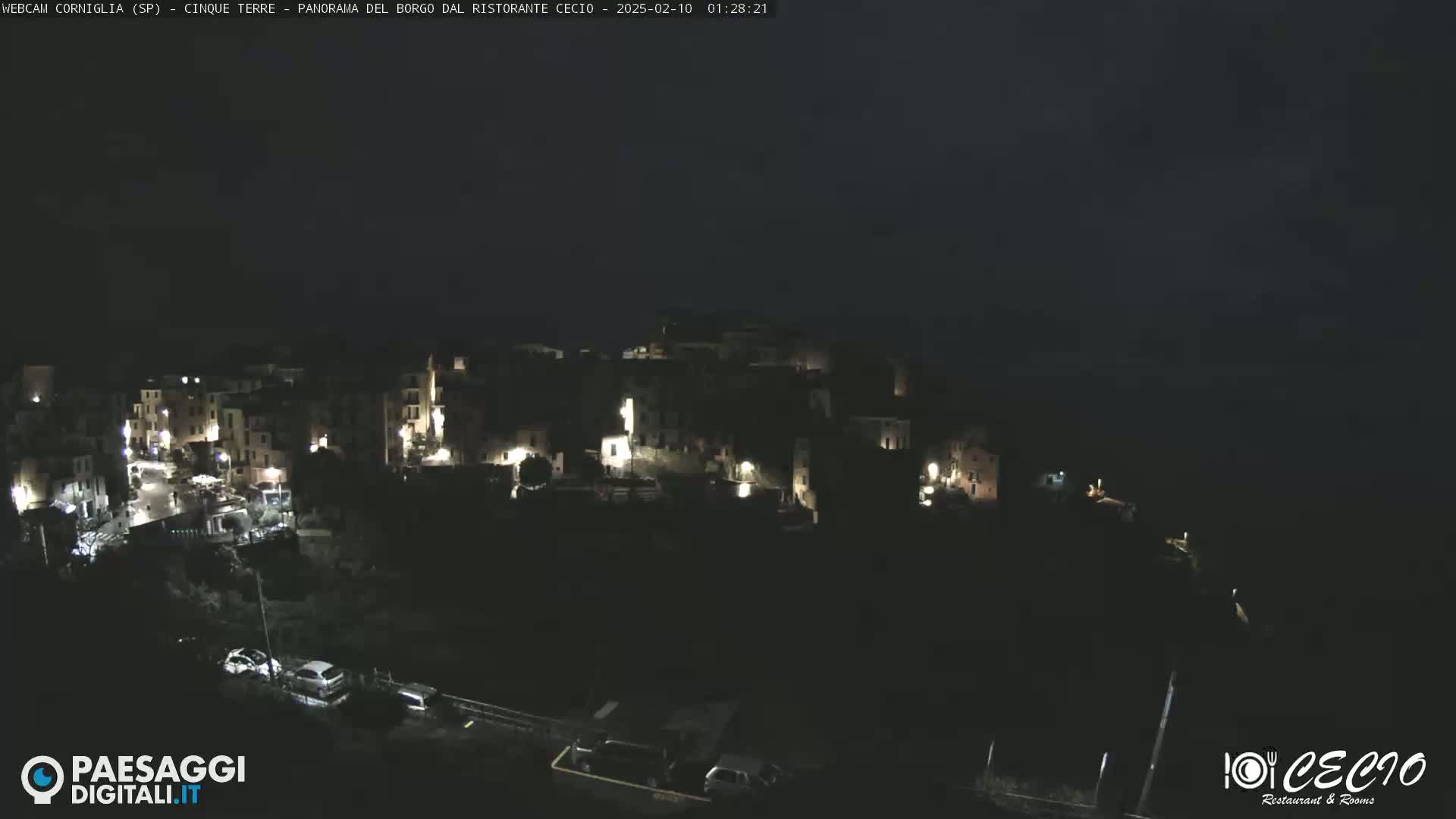 A nighttime, aerial view of a small, illuminated village nestled on a dark hillside.