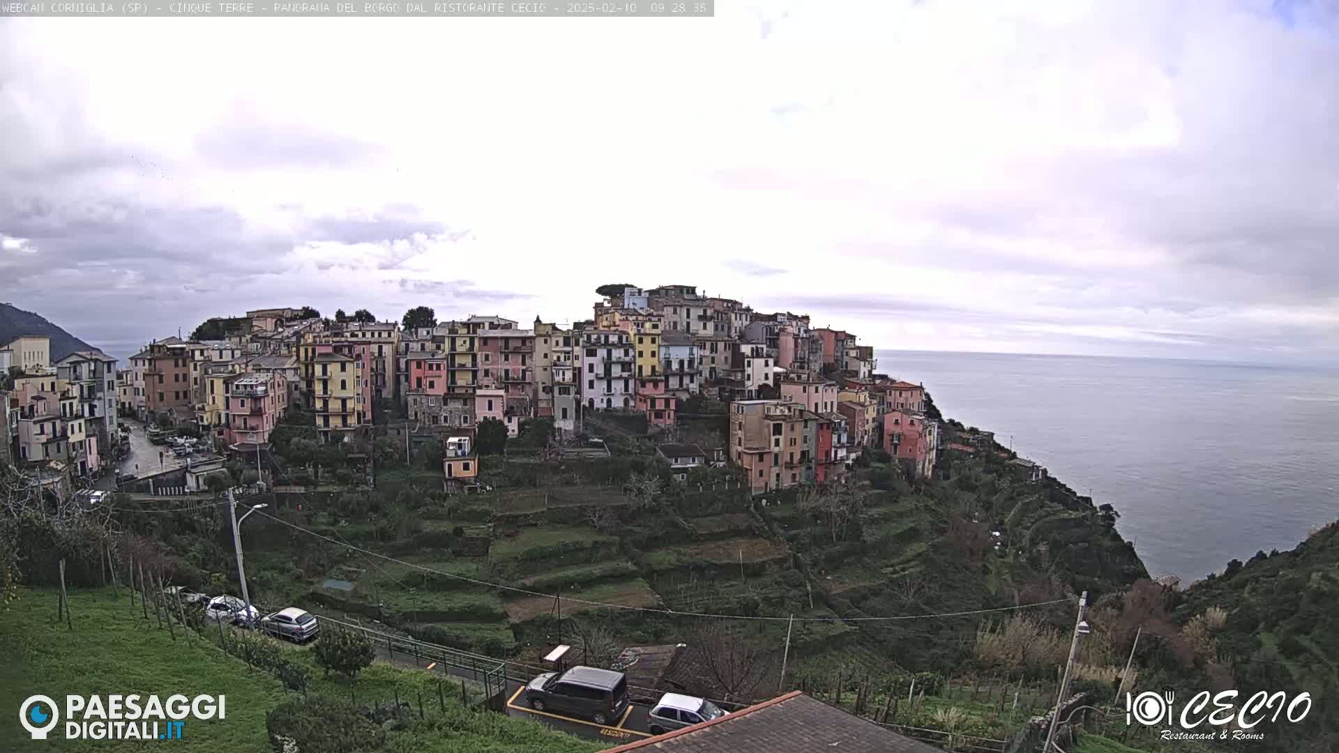 A hillside village of colorful buildings overlooks a calm sea under an overcast sky.