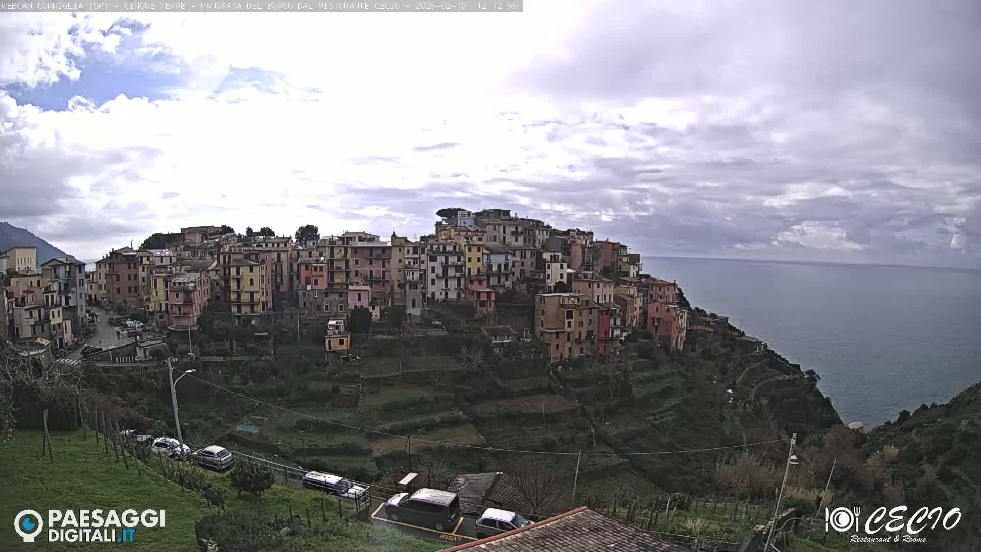 A hillside village of colorful buildings overlooks a calm ocean under a cloudy sky.