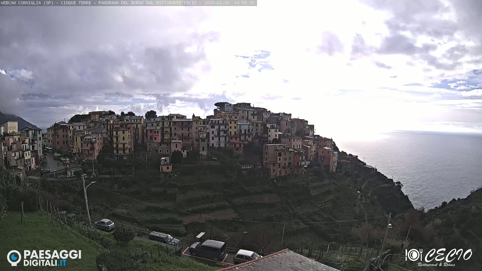 A hillside village of colorful buildings overlooks a calm ocean under a partly cloudy sky.