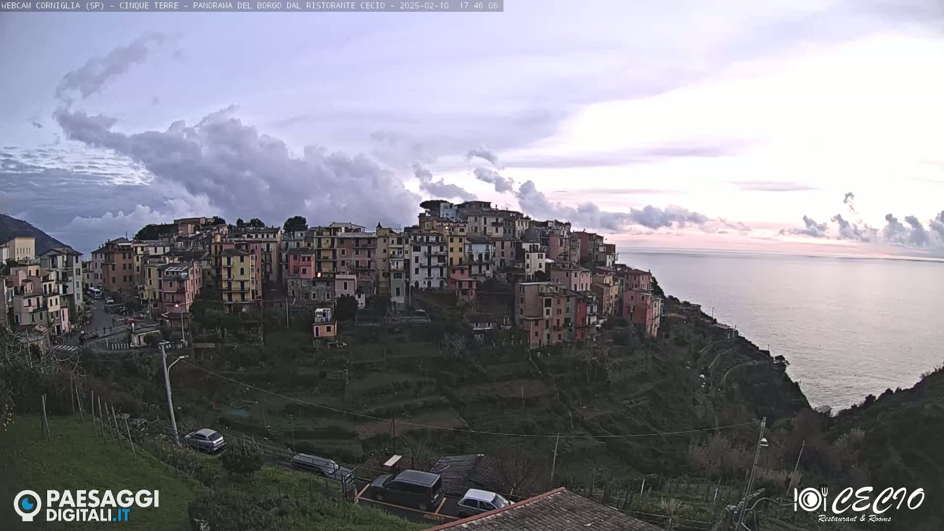 A colorful hillside village overlooks a calm sea under a partly cloudy sky.