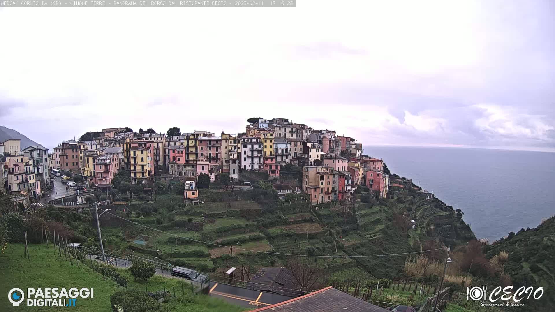 A colorful hillside village overlooks a calm sea under an overcast sky.