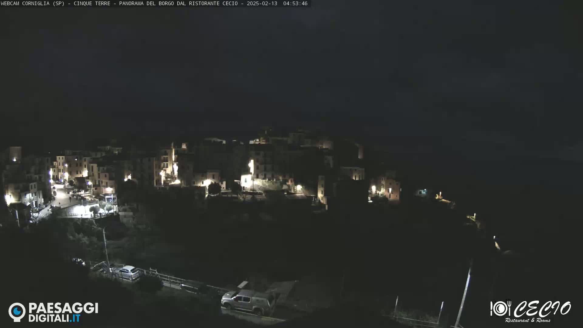 A nighttime, high-angle view of a small, dimly lit town nestled on a hillside.