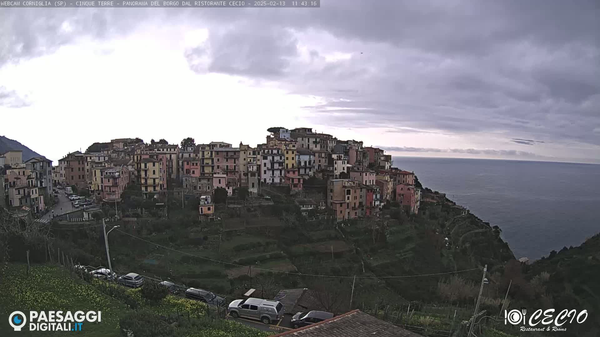 A hillside village of colorful buildings overlooks a calm sea under a cloudy sky.