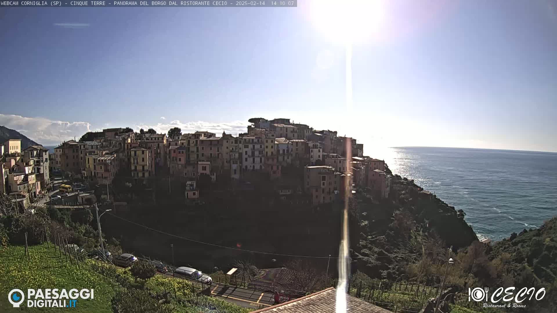 A sunny day overlooking a colorful hillside village perched on a cliff above a calm ocean.