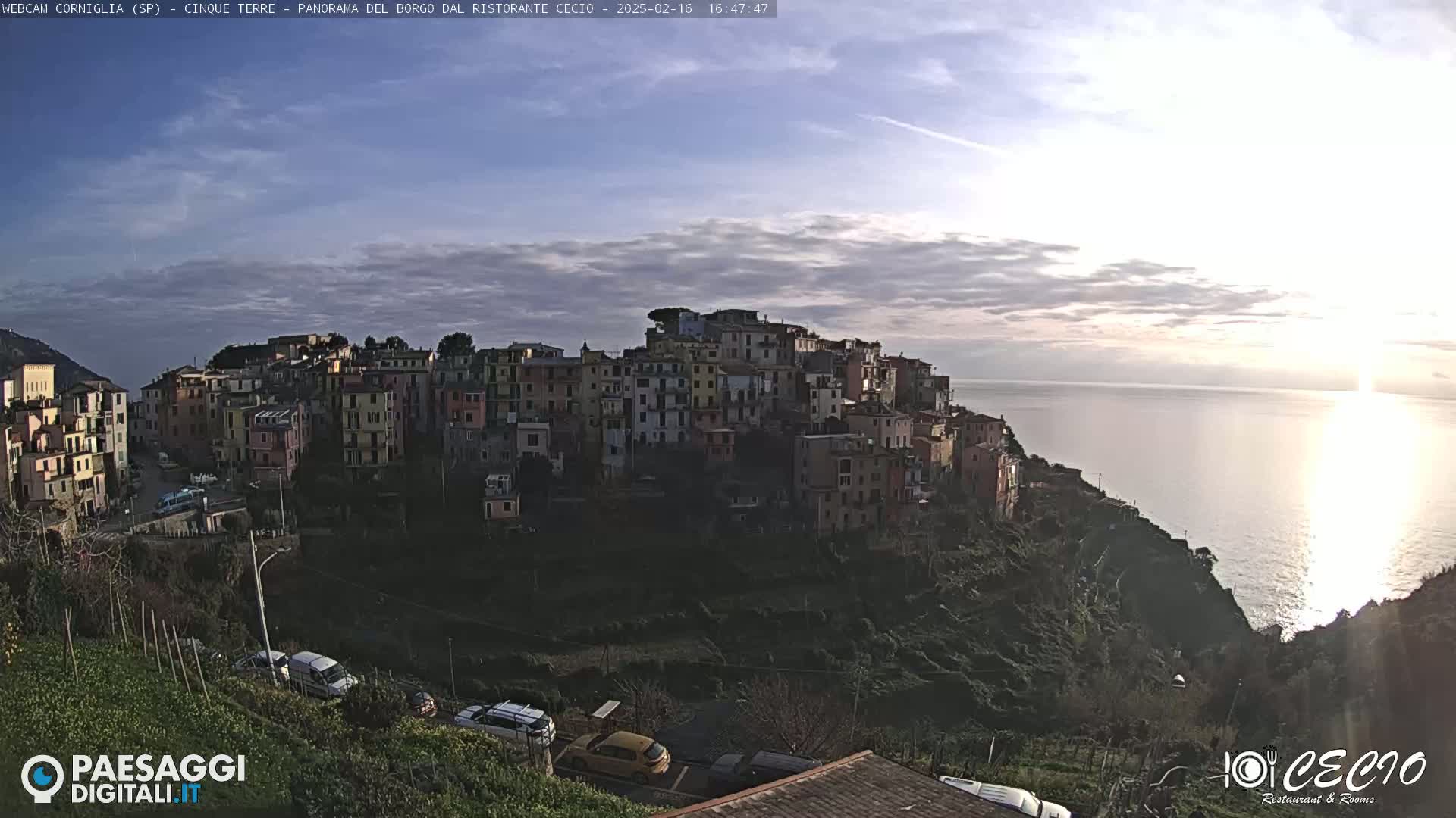 A coastal town of colorful buildings is perched on a cliff overlooking a calm sea under a partly cloudy sky.