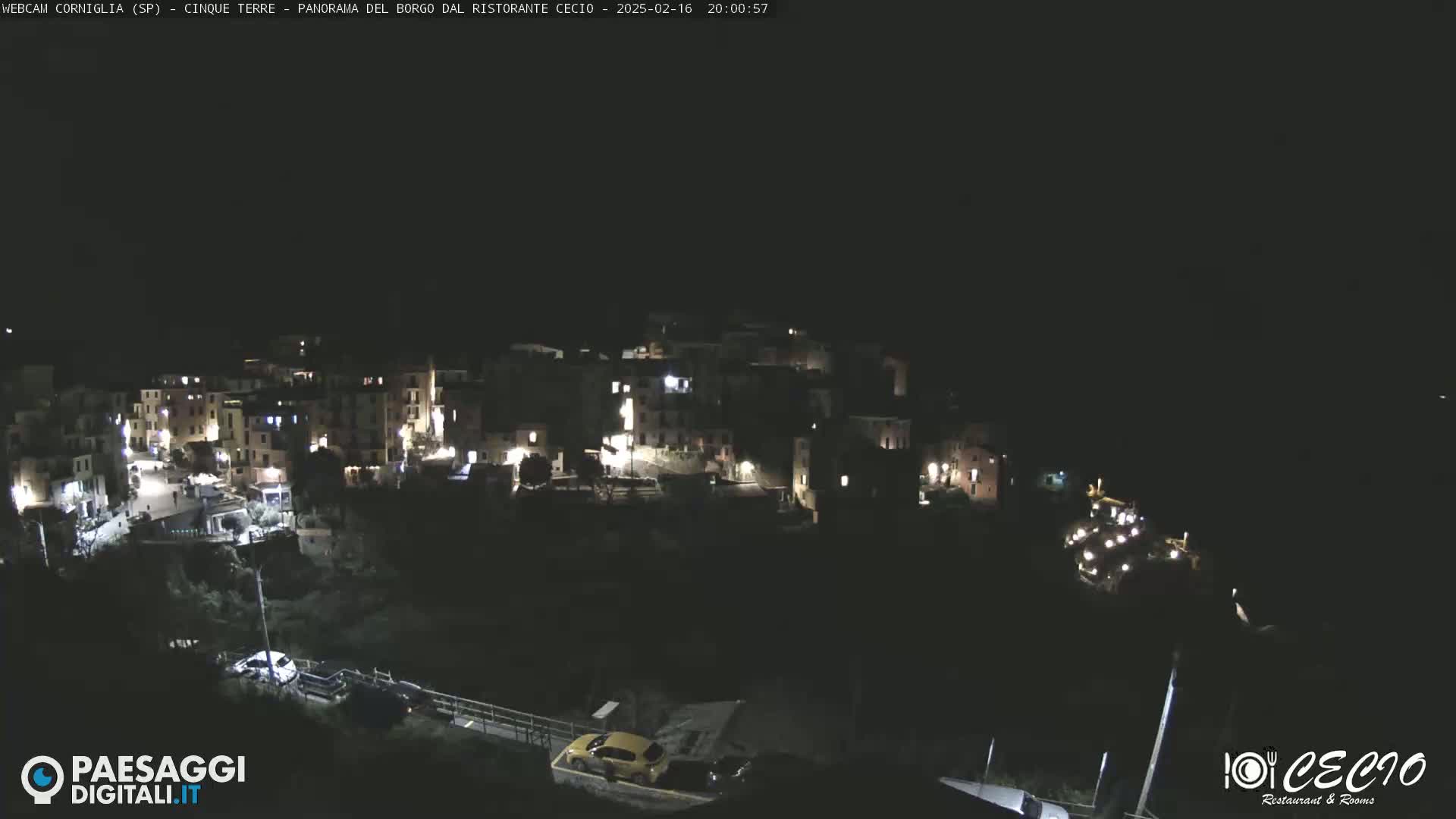 A nighttime, high-angle view of a small, illuminated village nestled on a hillside.