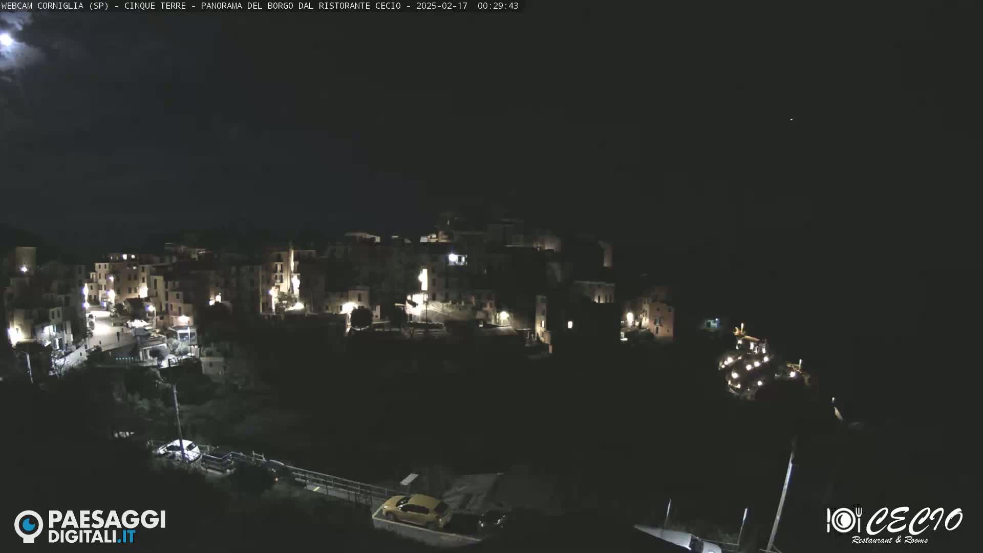 A nighttime, high-angle view shows a small, hilly town with scattered lights under a mostly clear, dark sky.