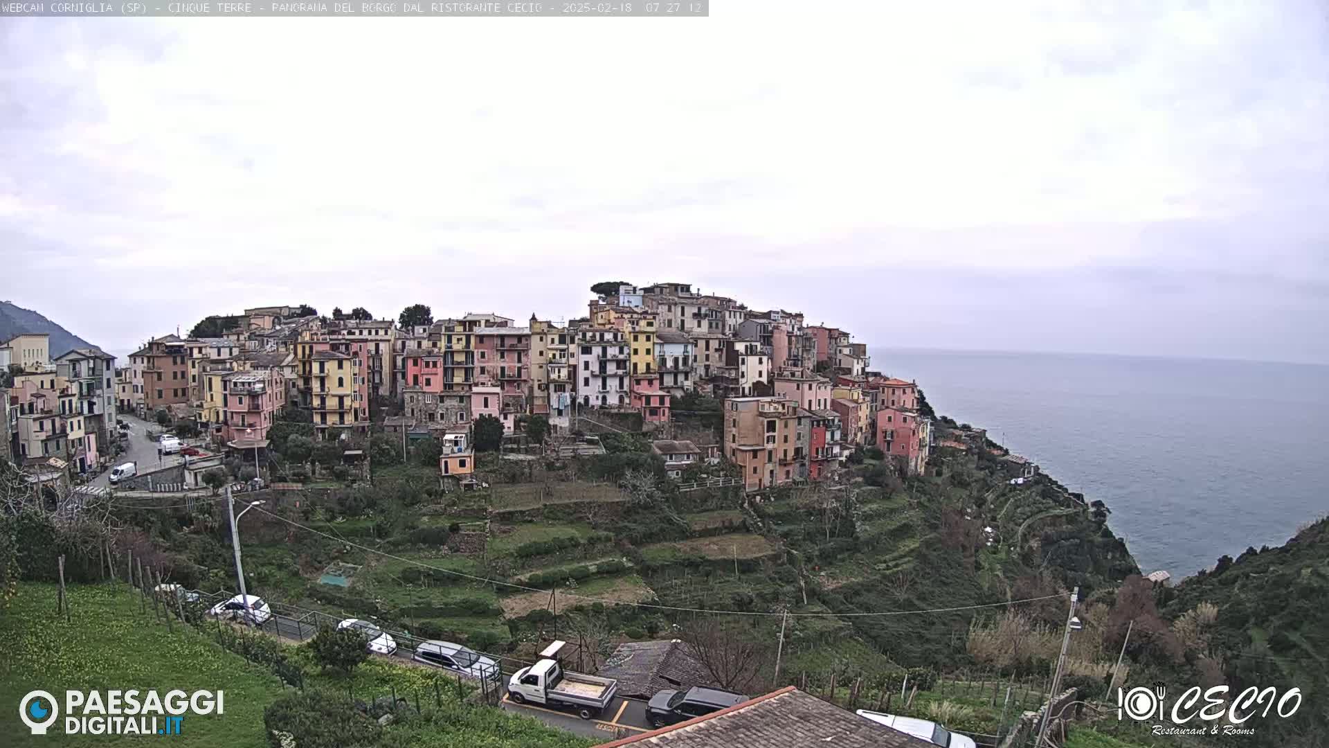 A hillside village of colorful buildings overlooks a calm sea under an overcast sky.