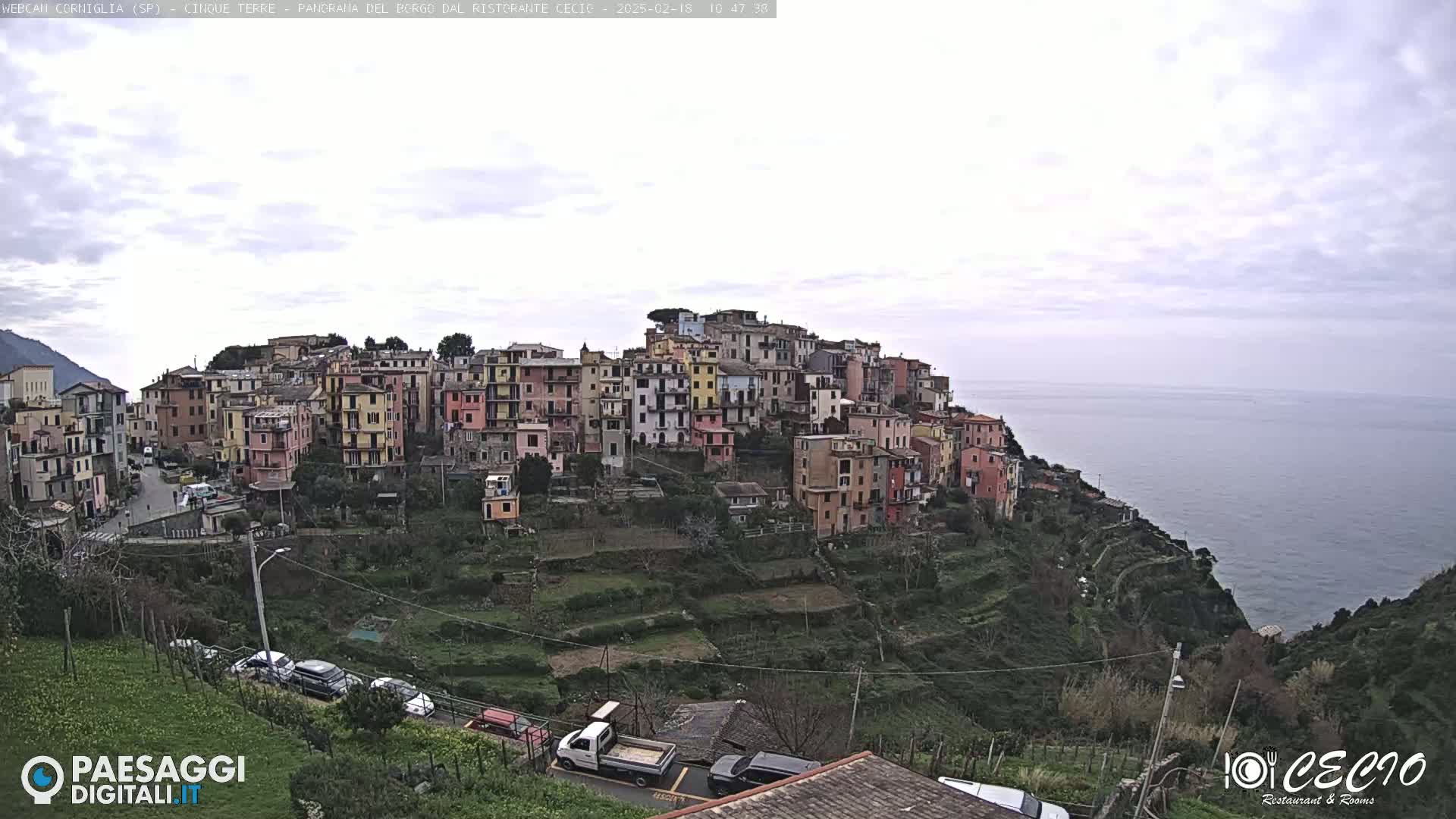 A colorful hillside village overlooks a calm sea under a cloudy sky.