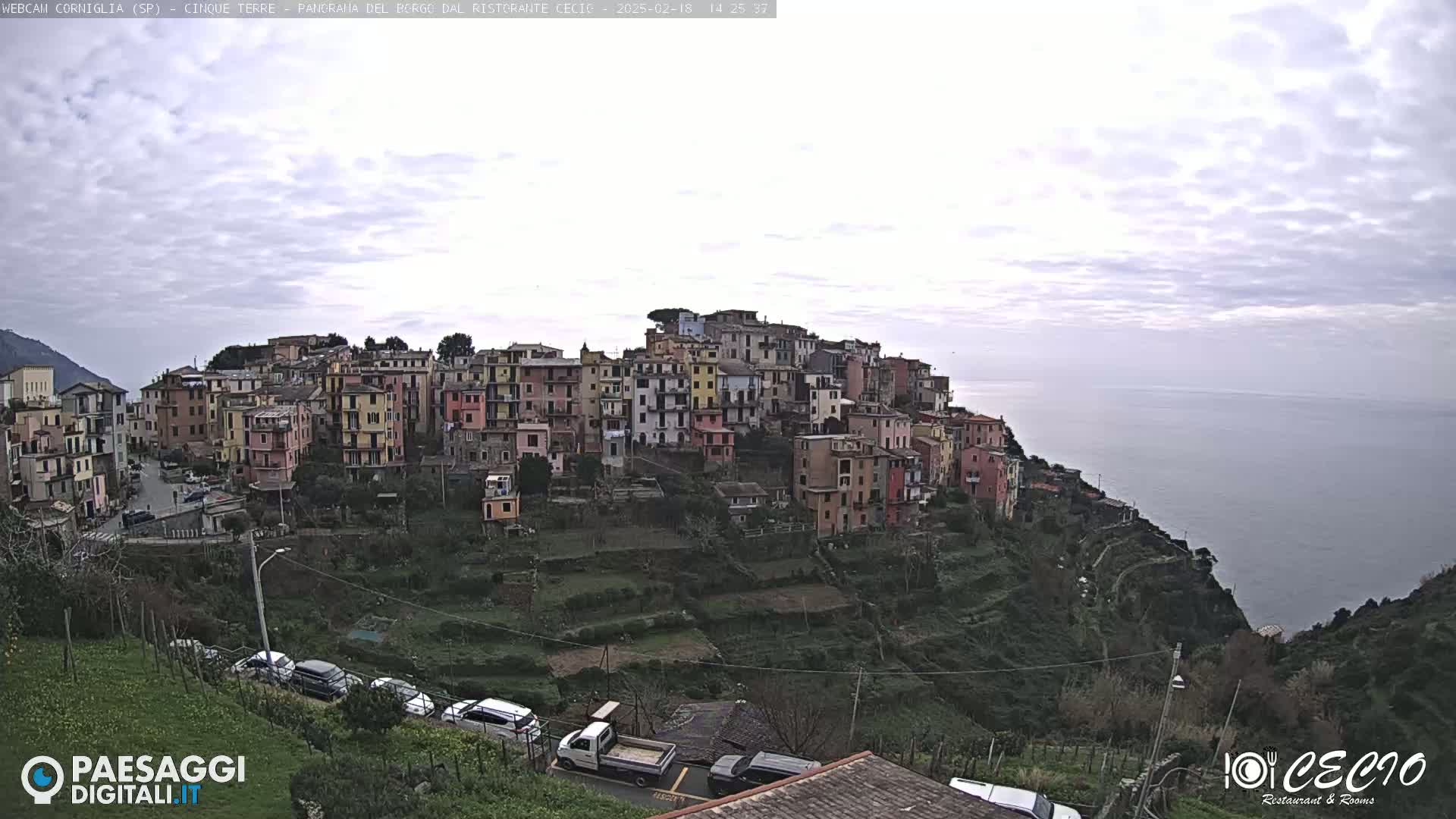 A coastal town of colorful buildings sits on a hillside overlooking a calm sea under an overcast sky.