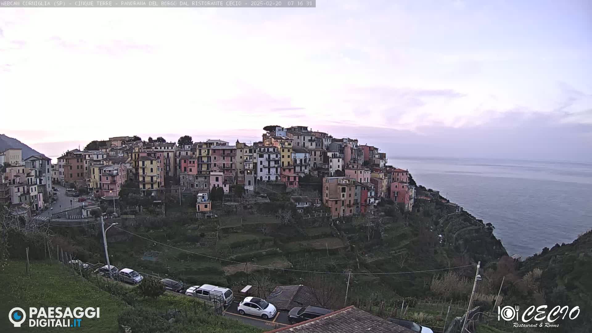 A hillside village of colorful buildings overlooks a calm sea under a pale, overcast sky.