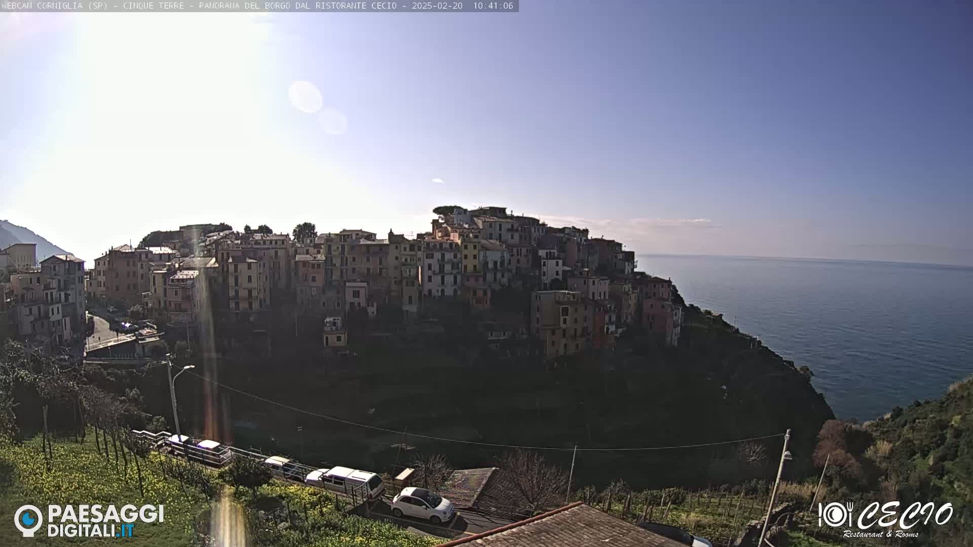 A sunny day overlooks a coastal village of colorful buildings clustered on a hillside, with a calm sea stretching to the horizon.