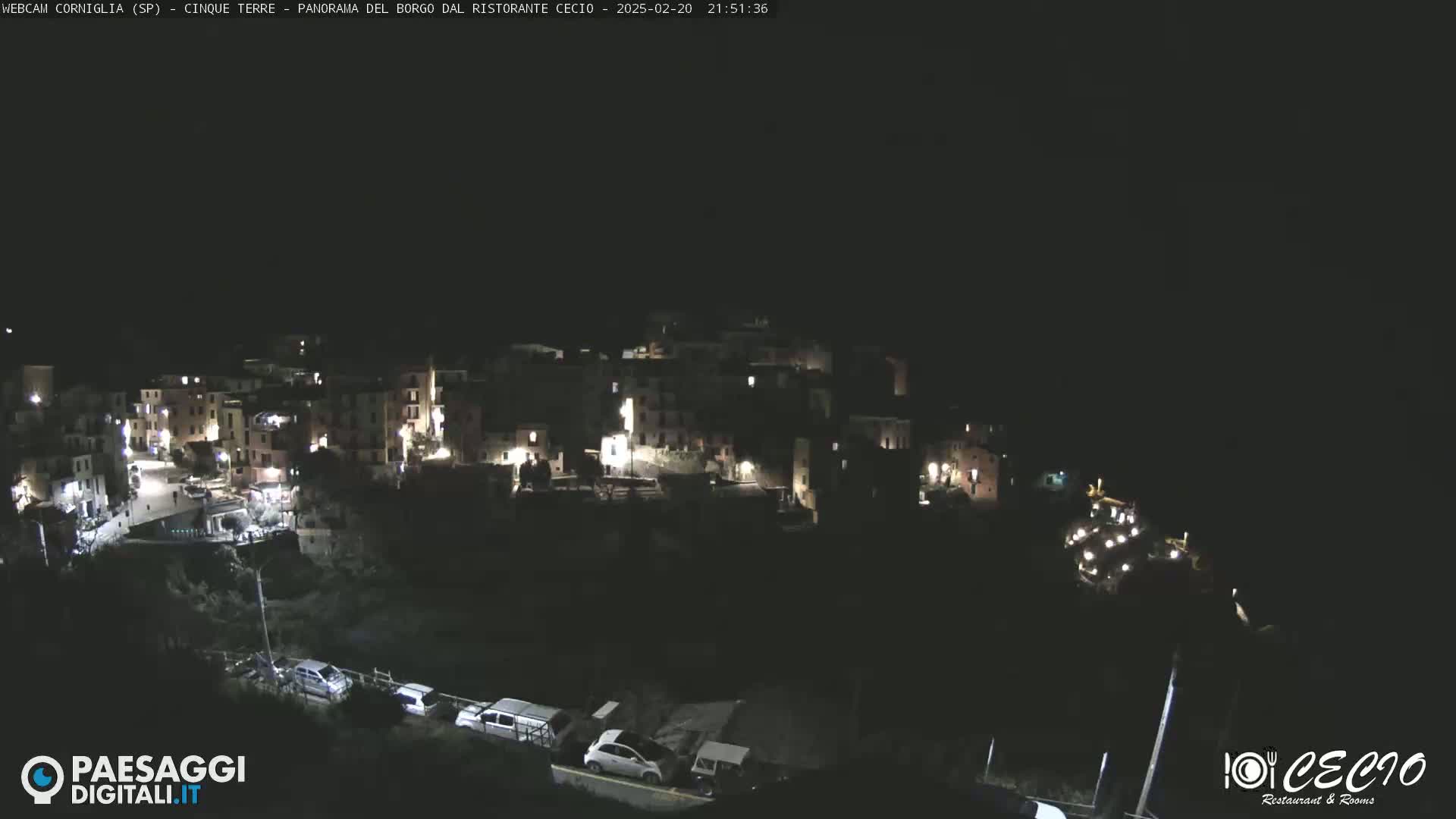 A nighttime, high-angle view of a small, illuminated village nestled on a dark hillside.