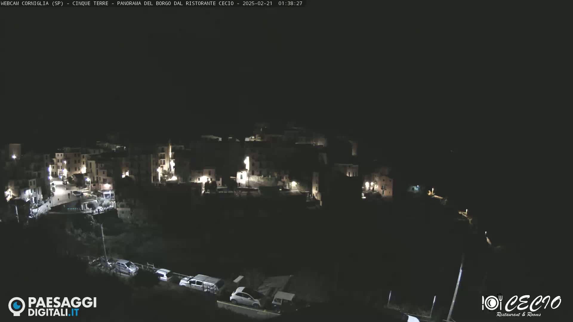 A nighttime, high-angle view of a small, dimly lit village nestled on a hillside.