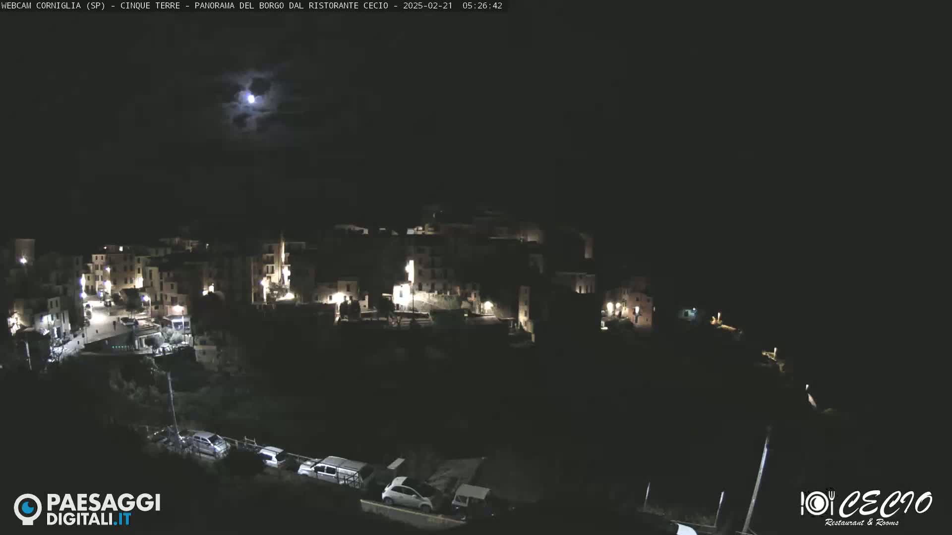 A nighttime, moonlit view of a small, illuminated village nestled on a hillside.