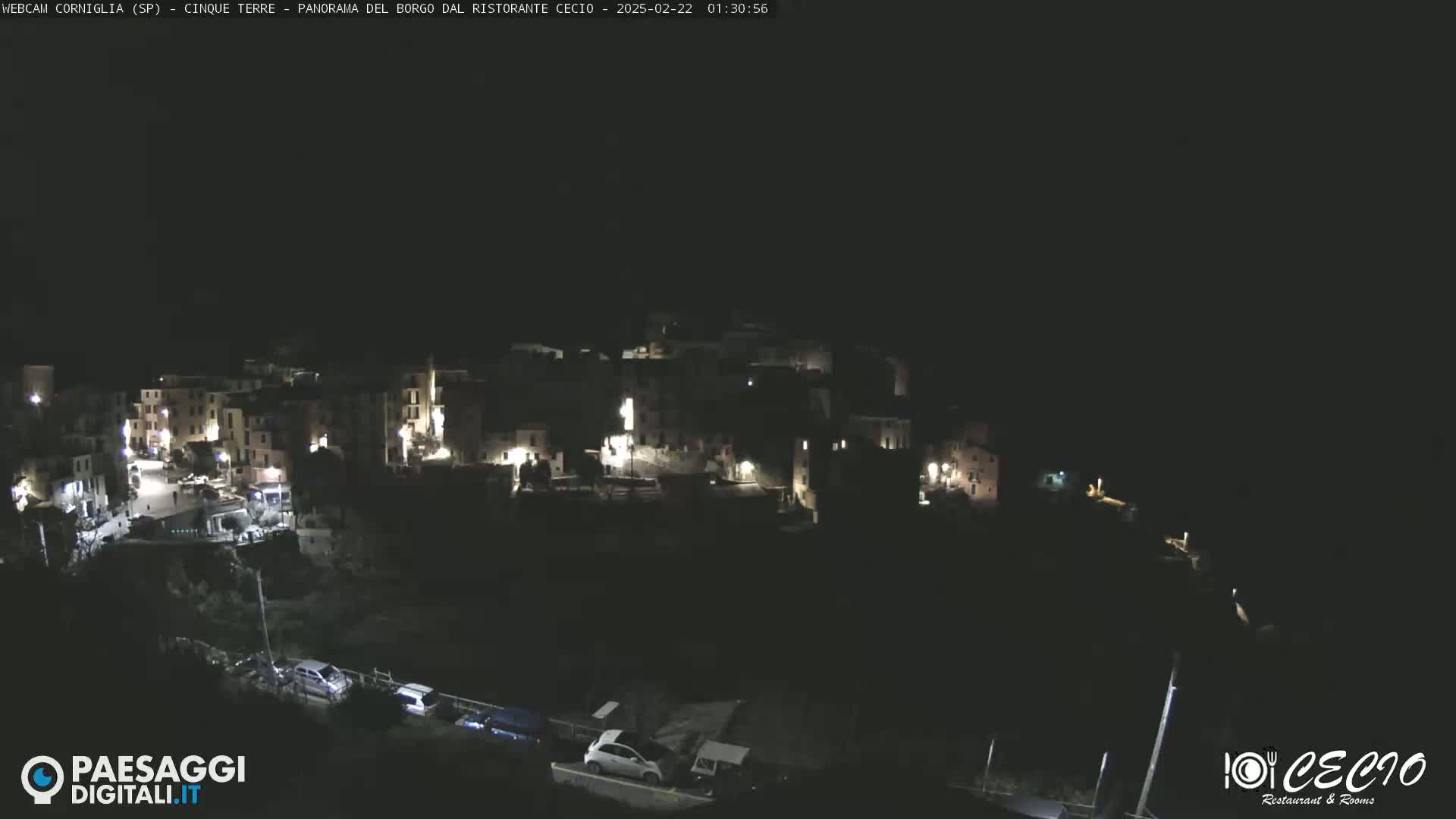 A nighttime, aerial view shows a small, dark town with sparsely lit buildings and a few cars on a road below.