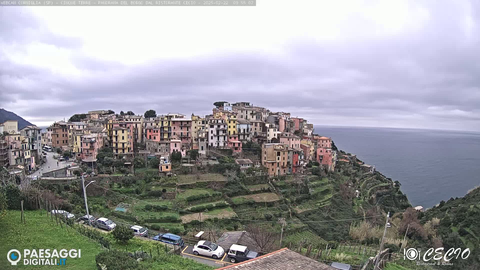 A colorful hillside village overlooks a calm sea under an overcast sky.