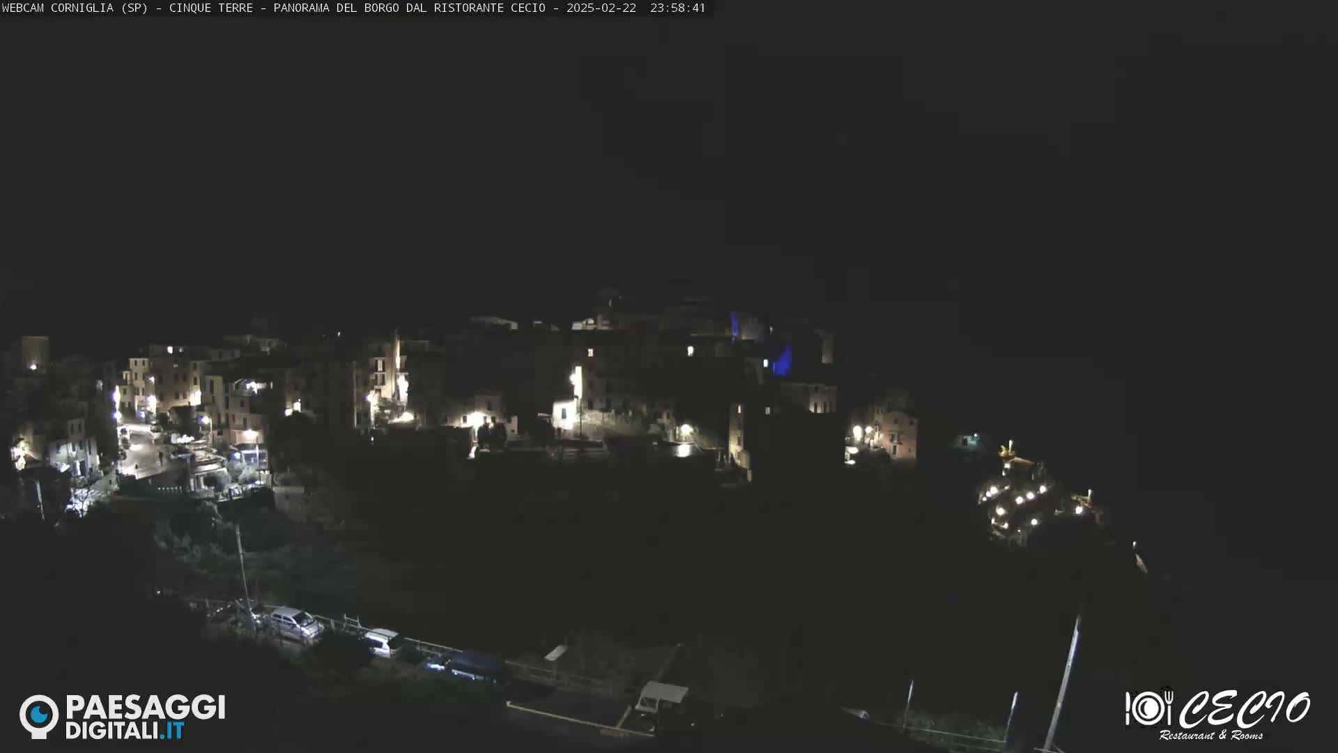 A nighttime, high-angle view shows a small, illuminated town nestled on a hillside.