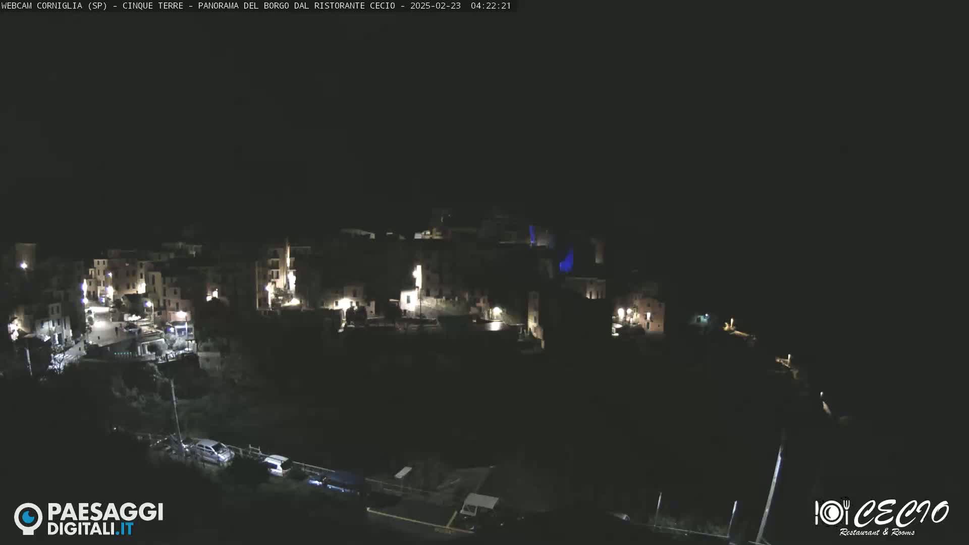 A nighttime, high-angle view shows a small, dimly lit town nestled on a hillside.