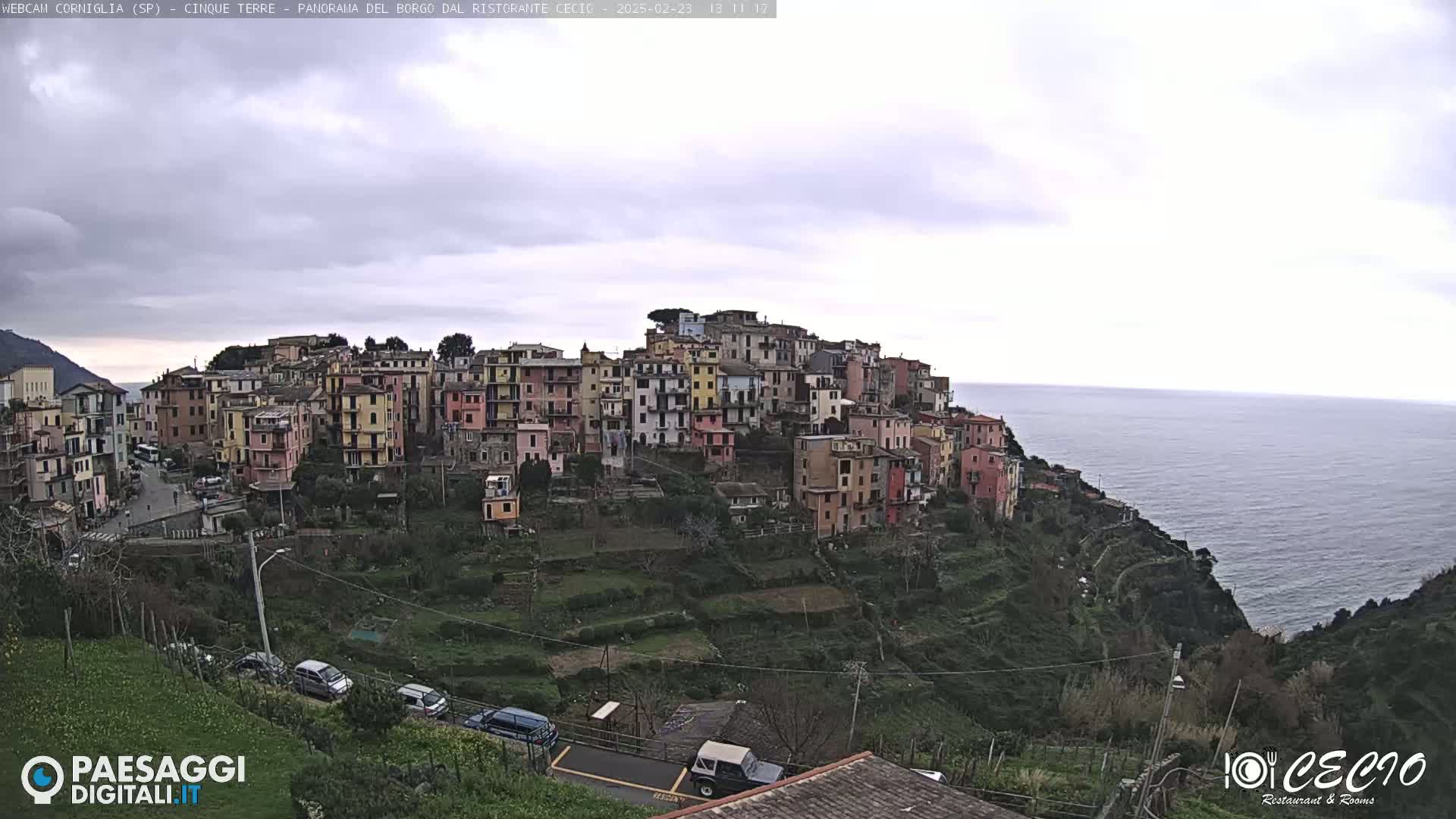 A colorful hillside village overlooks a calm sea under an overcast sky.