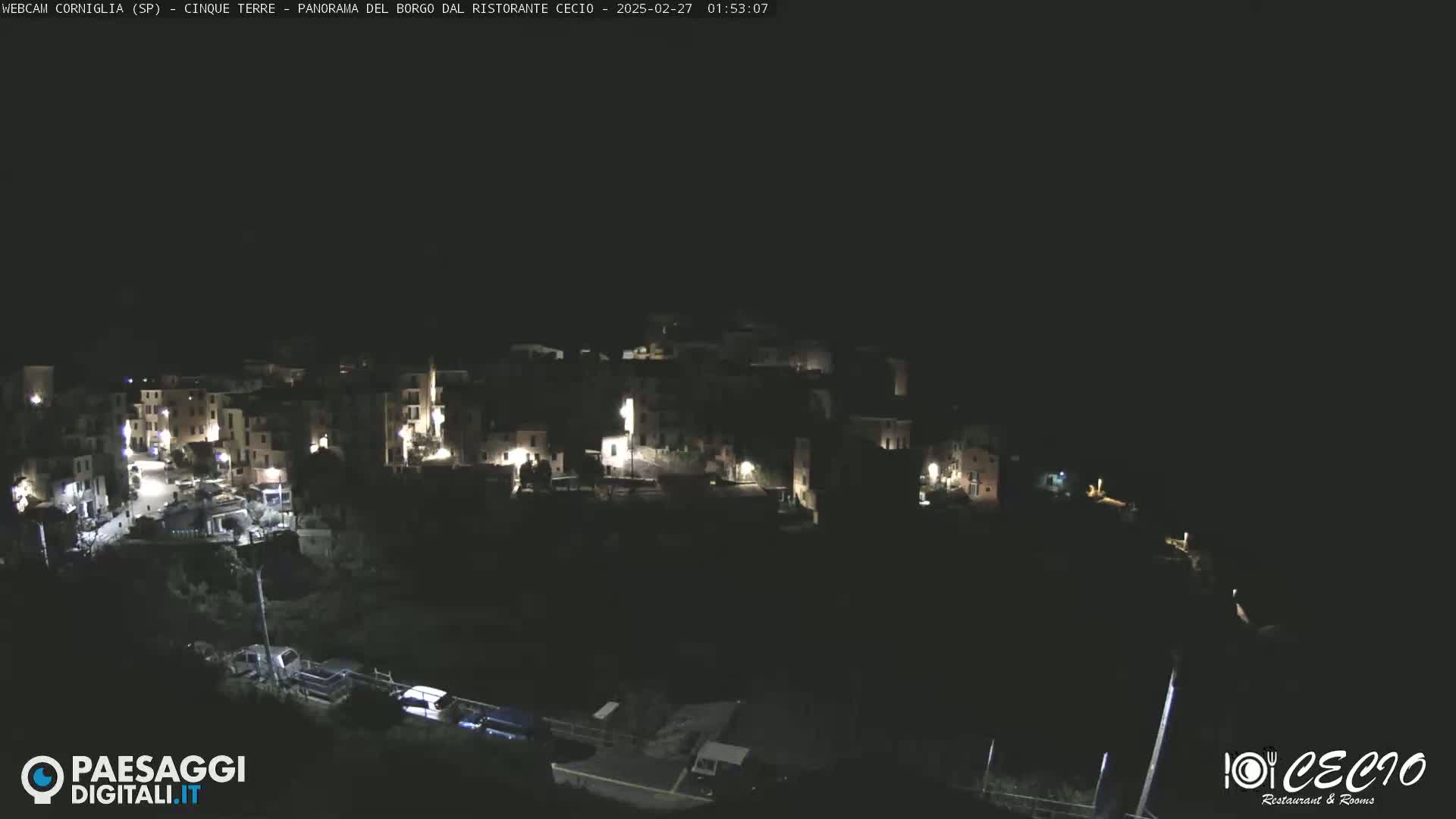 A nighttime, aerial view of a small, dimly lit town nestled on a hillside.
