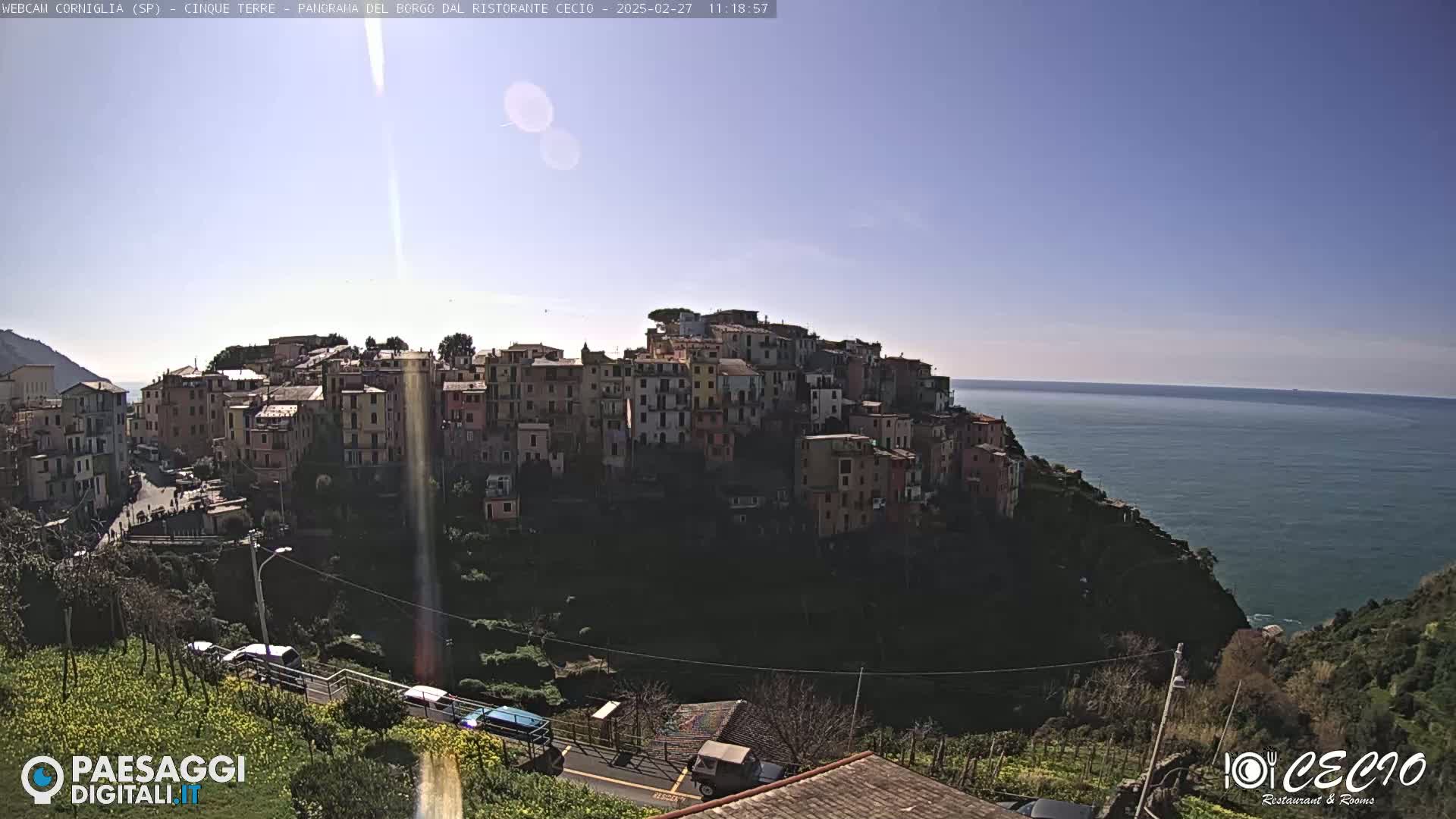 A hillside town of colorful buildings overlooks a calm blue sea under a clear, sunny sky.