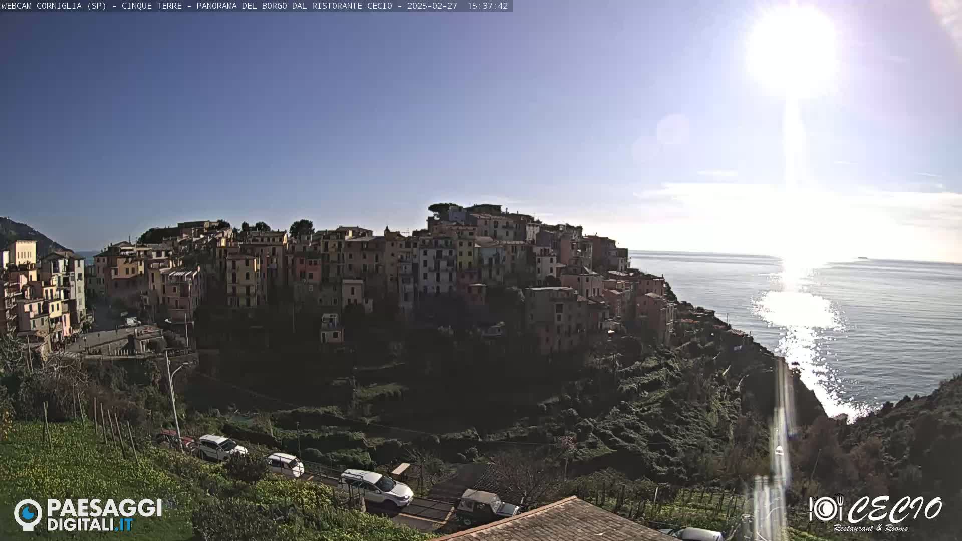A sunlit coastal town clings to a hillside overlooking a sparkling sea under a mostly clear sky.