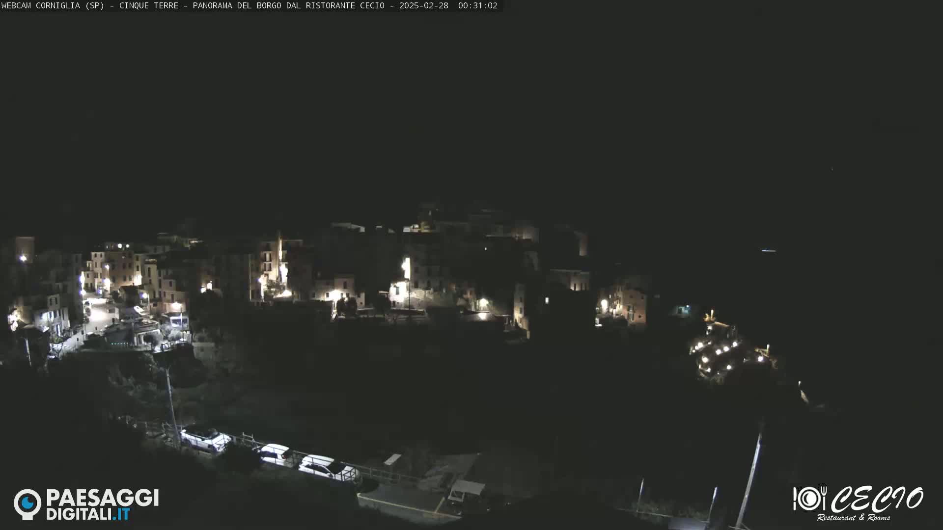 A nighttime, high-angle view of a small, dimly lit town nestled on a hillside.