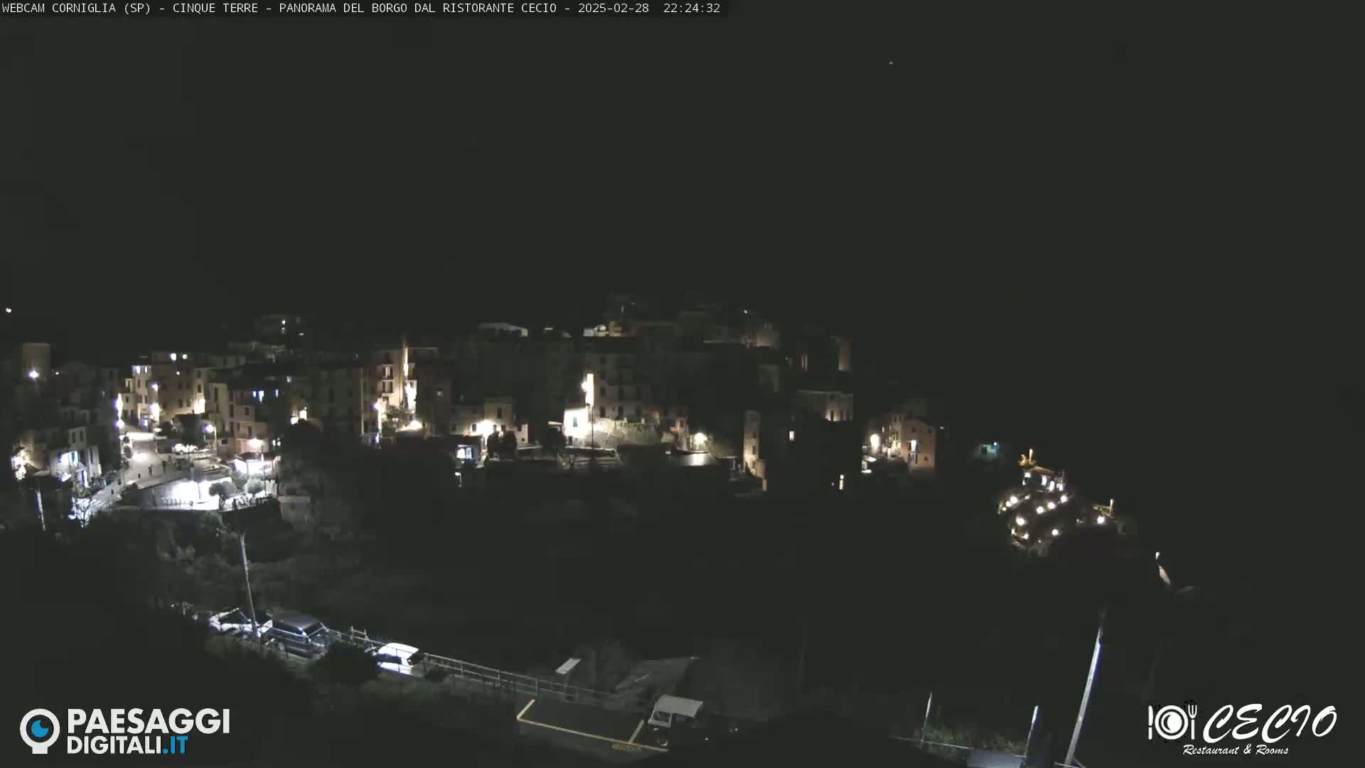A nighttime, high-angle view shows a small, illuminated town nestled on a hillside.