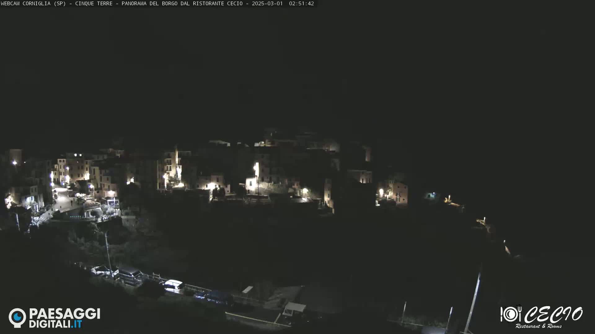 A nighttime, high-angle view of a small, dimly lit town nestled on a hillside.