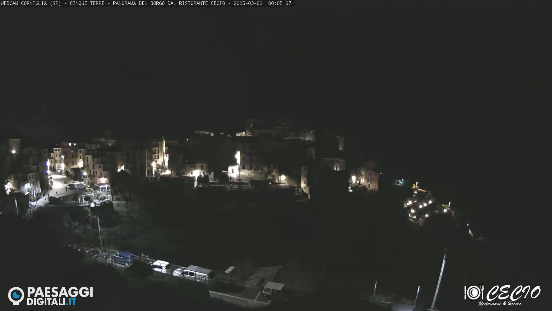 A nighttime, high-angle view of a small, illuminated town nestled on a hillside.