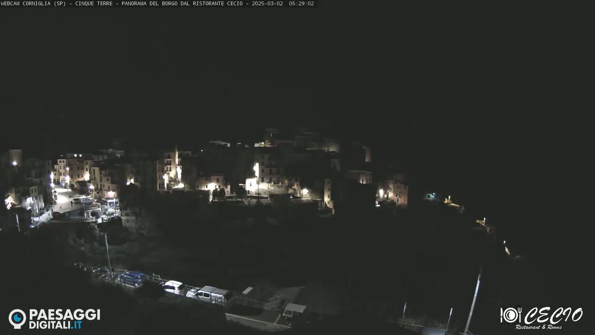 A nighttime, aerial view shows a small, illuminated town nestled on a dark hillside.
