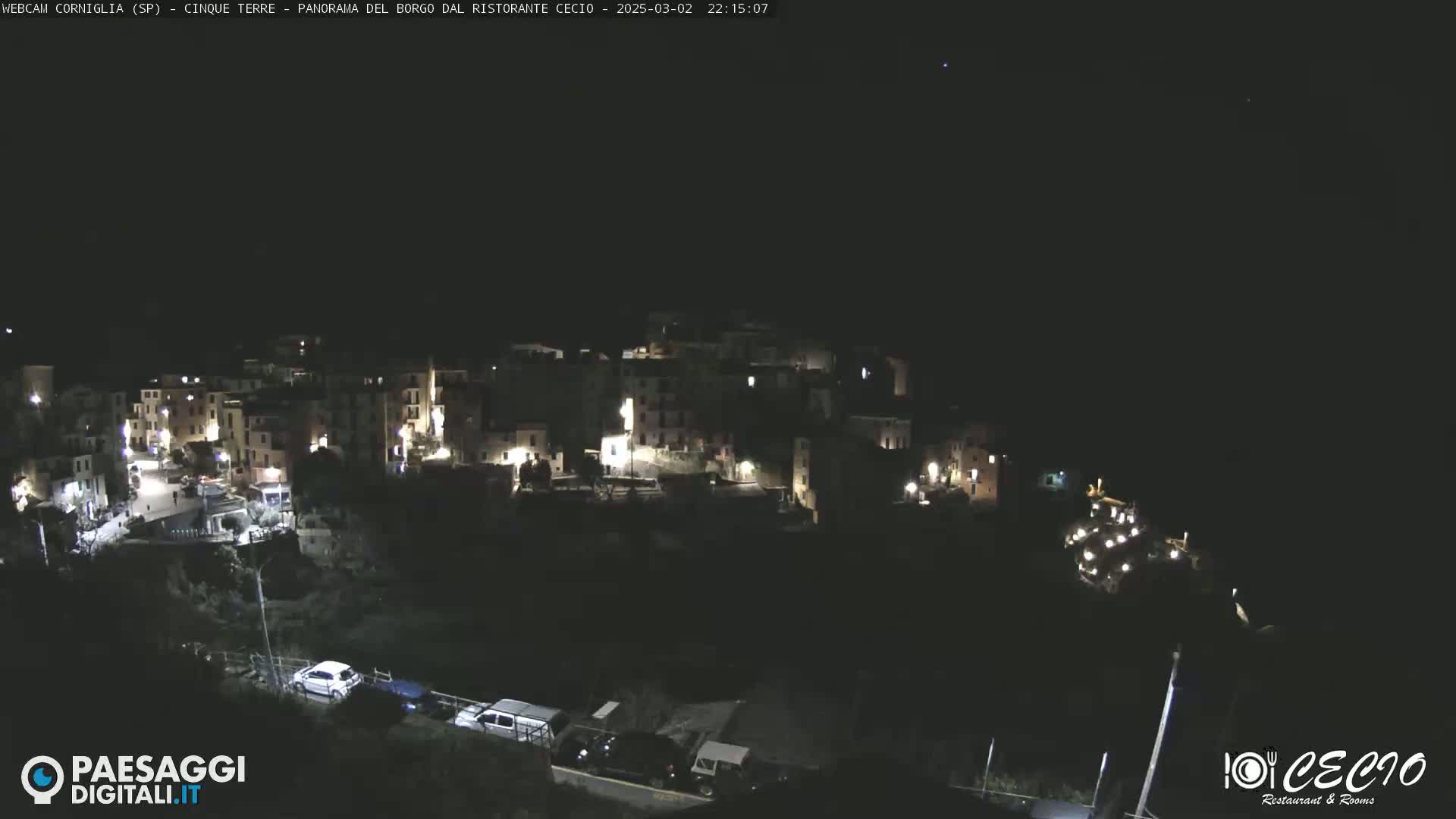 A nighttime, high-angle view shows a small, illuminated town nestled on a dark hillside.