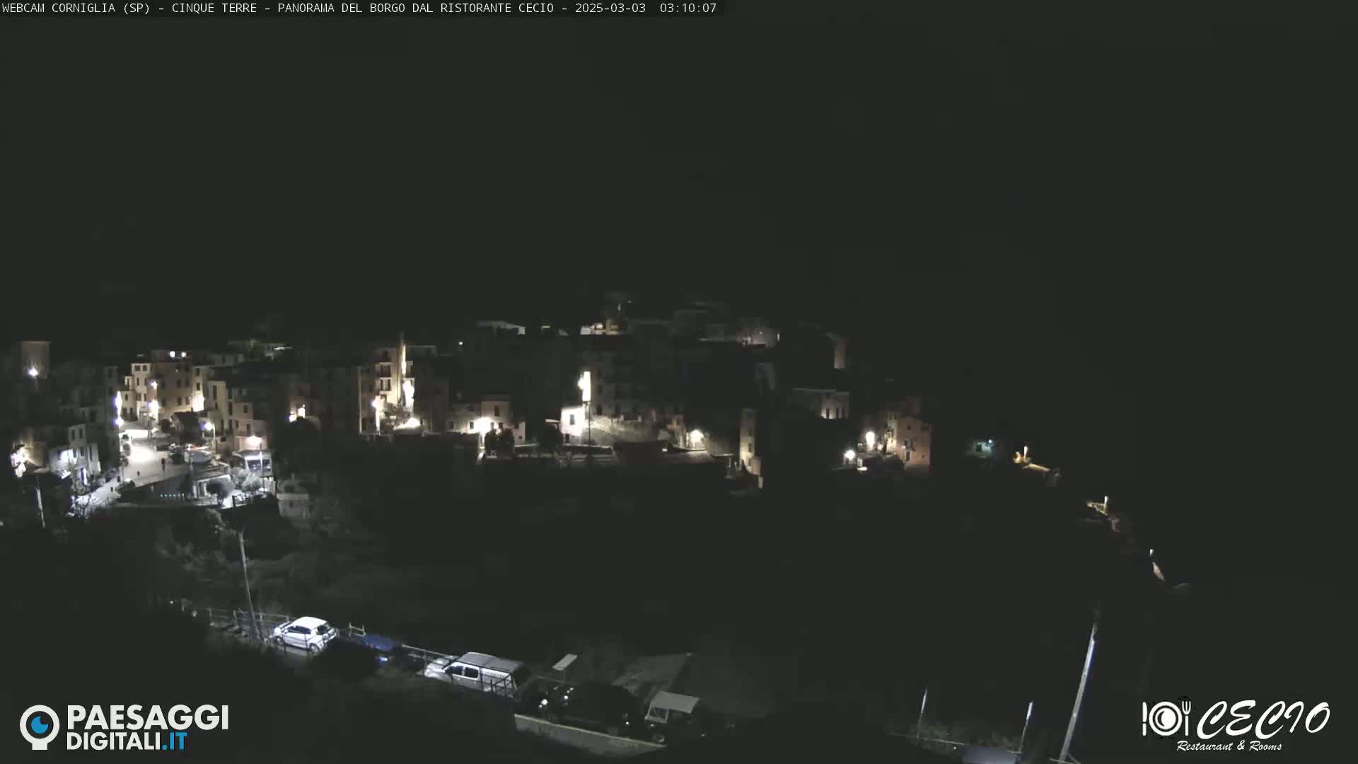 A nighttime, aerial view of a small, illuminated town nestled on a hillside under a dark sky.