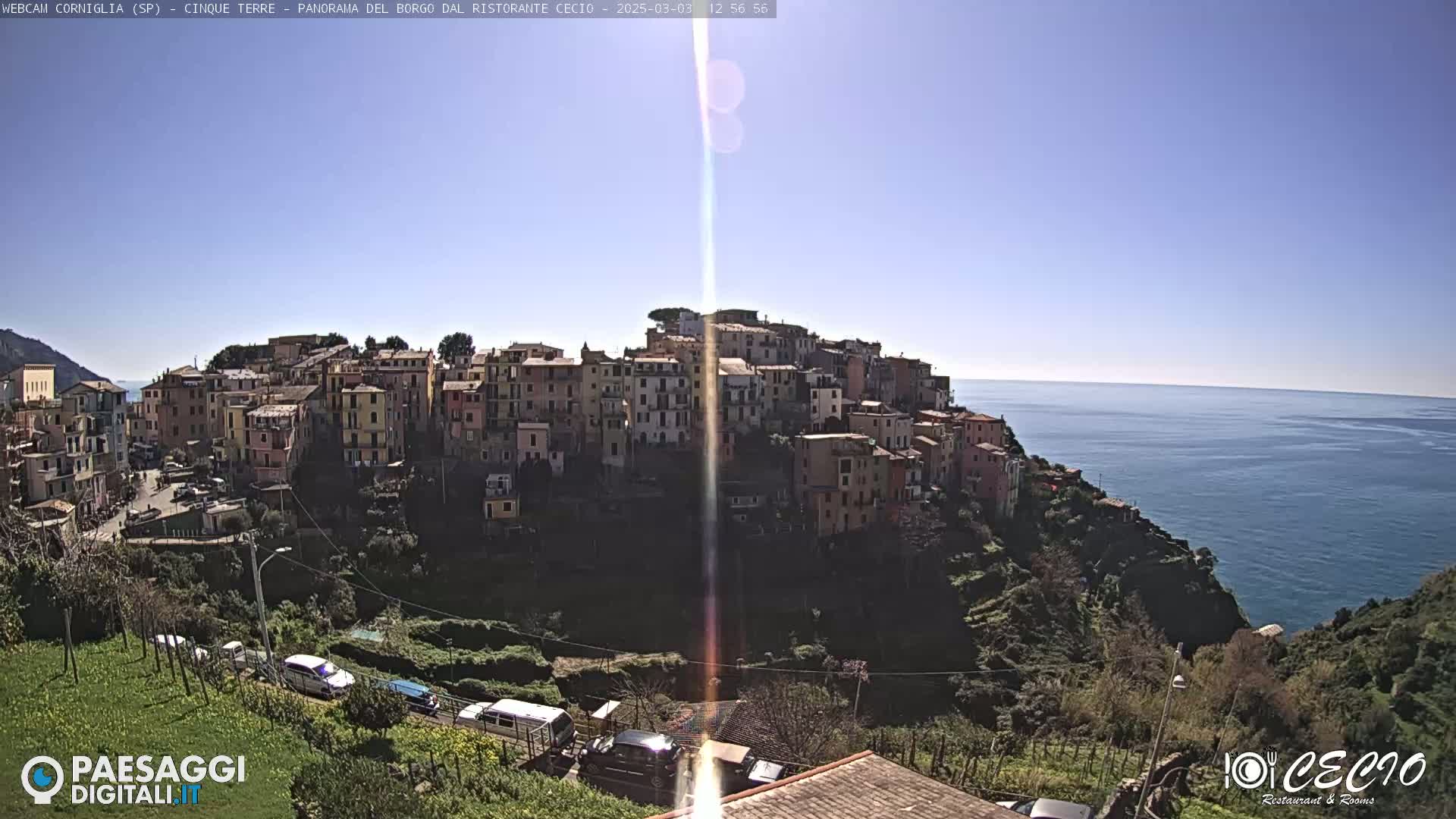 A coastal village of colorful buildings clings to a hillside overlooking a calm blue sea under a clear, sunny sky.