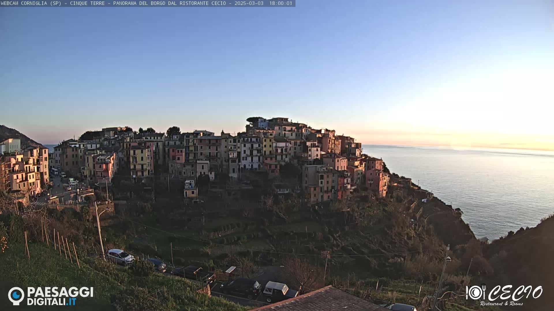 A colorful village perched on a cliff overlooking a calm sea at sunset.