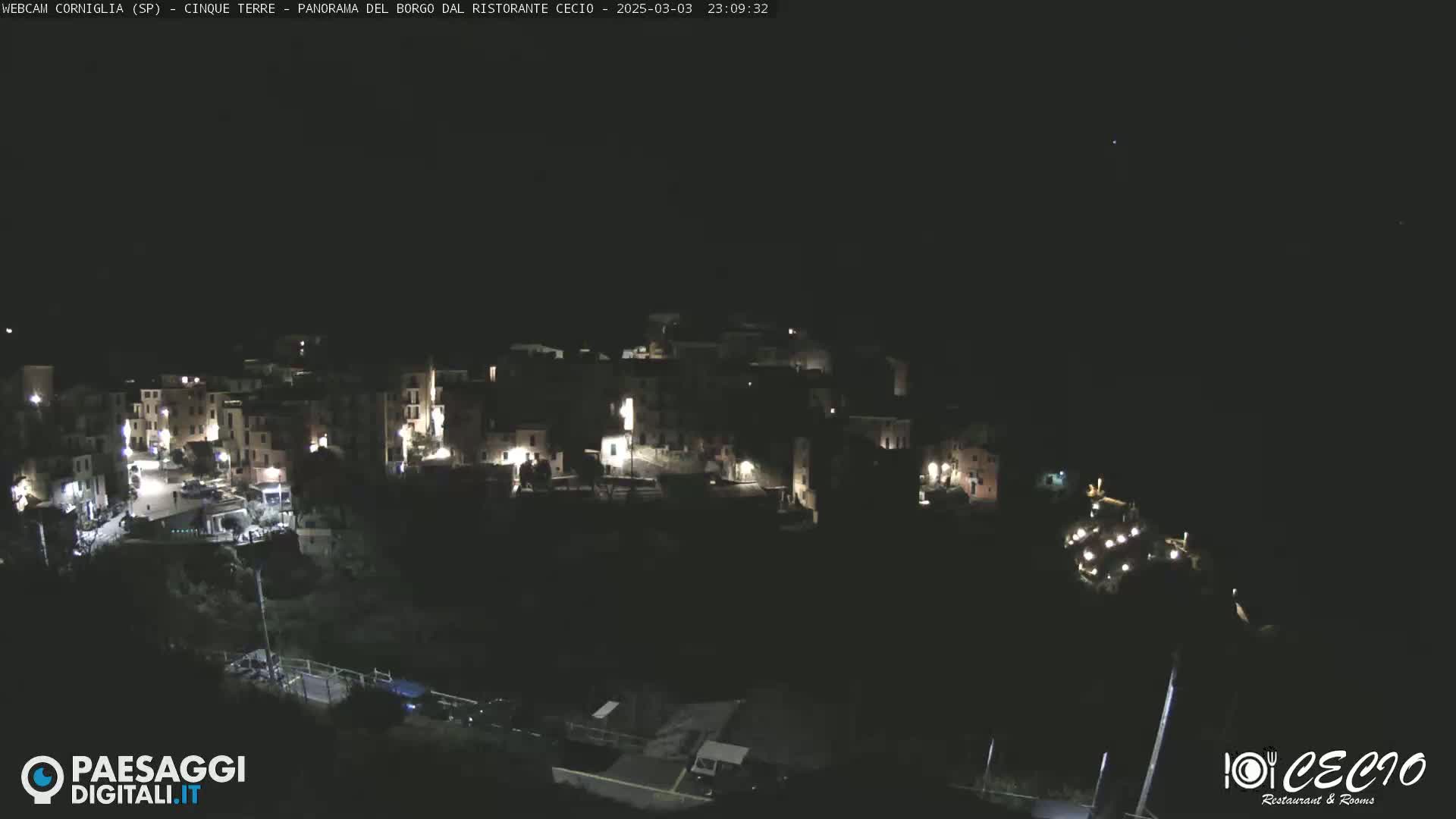 A nighttime, aerial view of a small, illuminated town nestled on a hillside under a clear, dark sky.