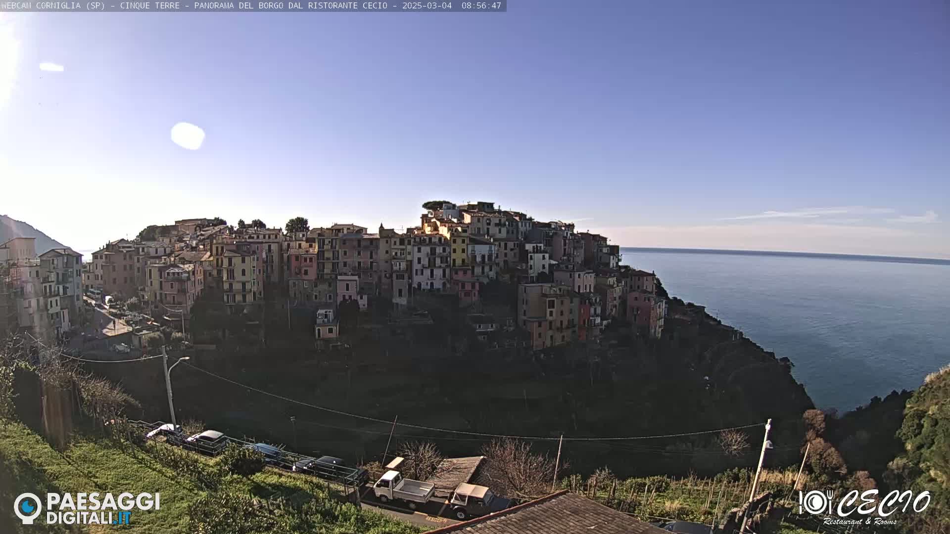 A colorful hillside village overlooks a calm, blue ocean under a clear, sunny sky.