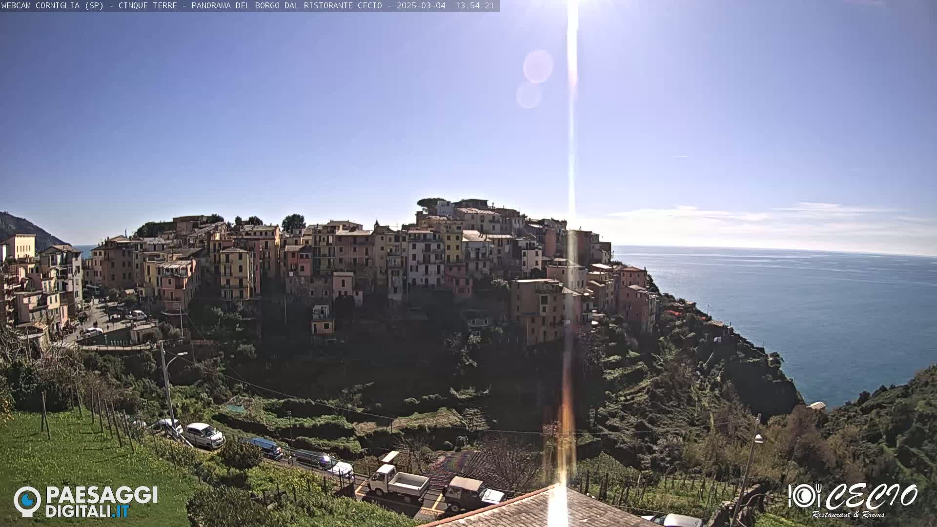 A colorful hillside village overlooks a calm ocean under a bright, sunny sky.