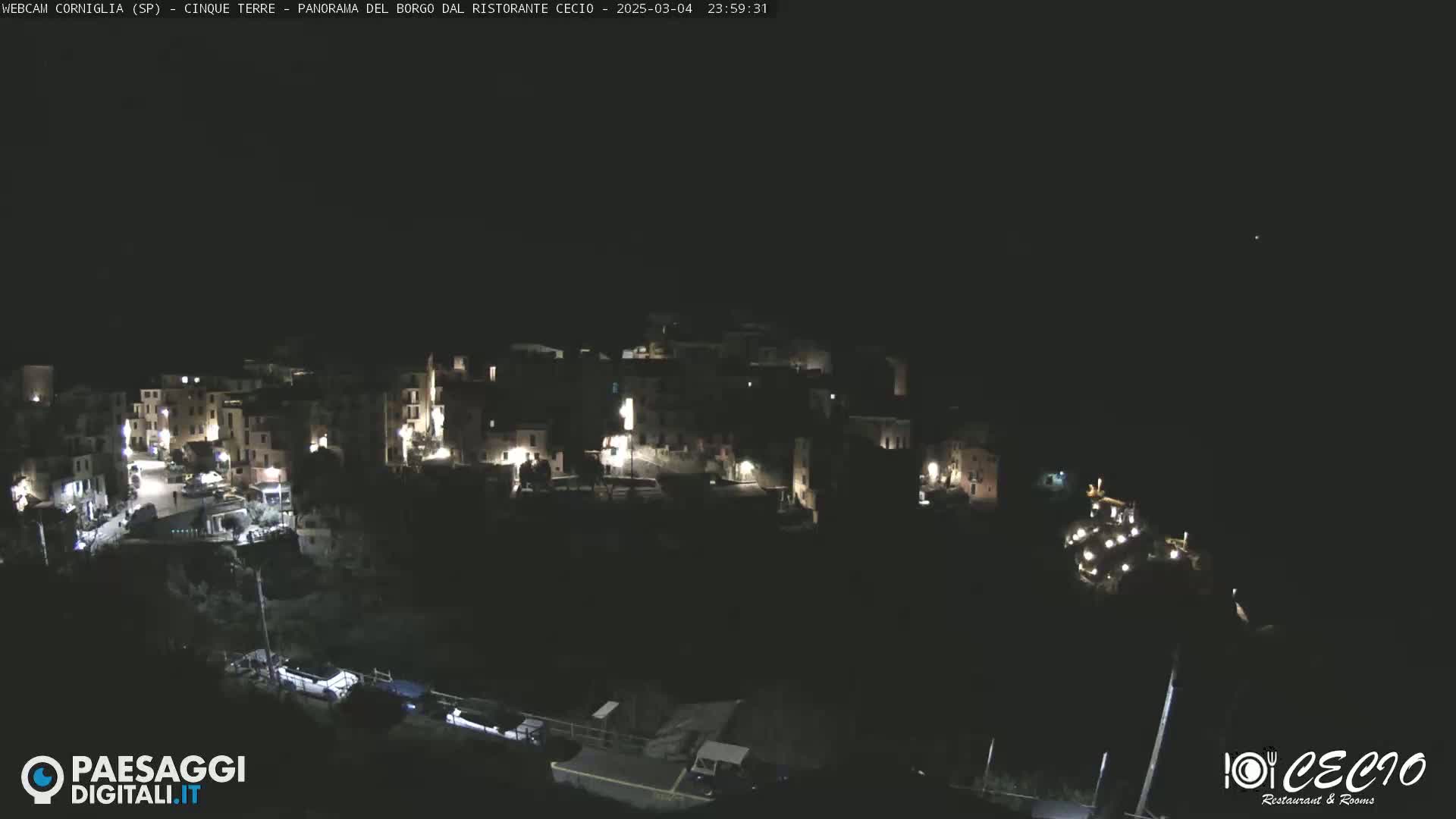 A nighttime, high-angle view of a small, illuminated village nestled into a dark hillside.