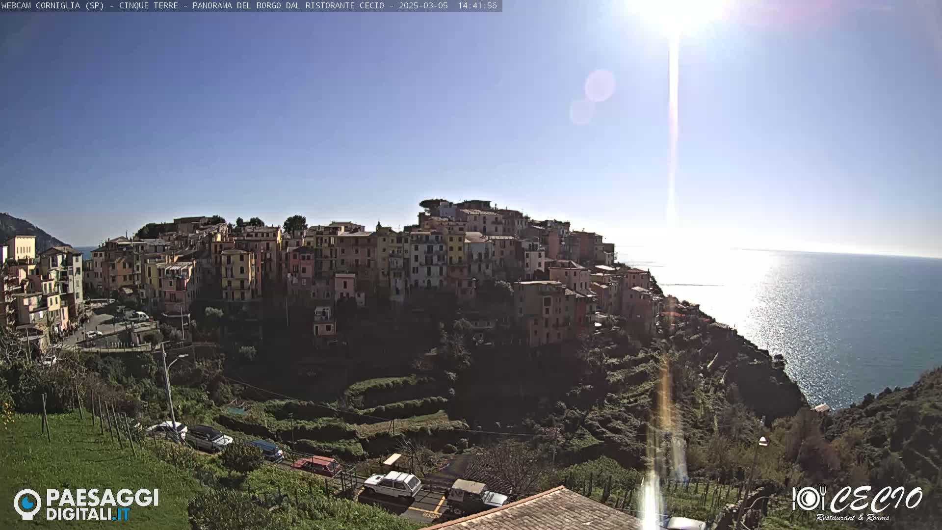 A sunny coastal village of colorful buildings on a hillside overlooking a sparkling blue sea.