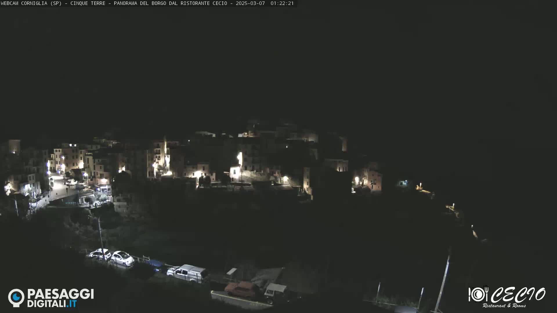 A nighttime, aerial view shows a small, illuminated town nestled on a dark hillside.