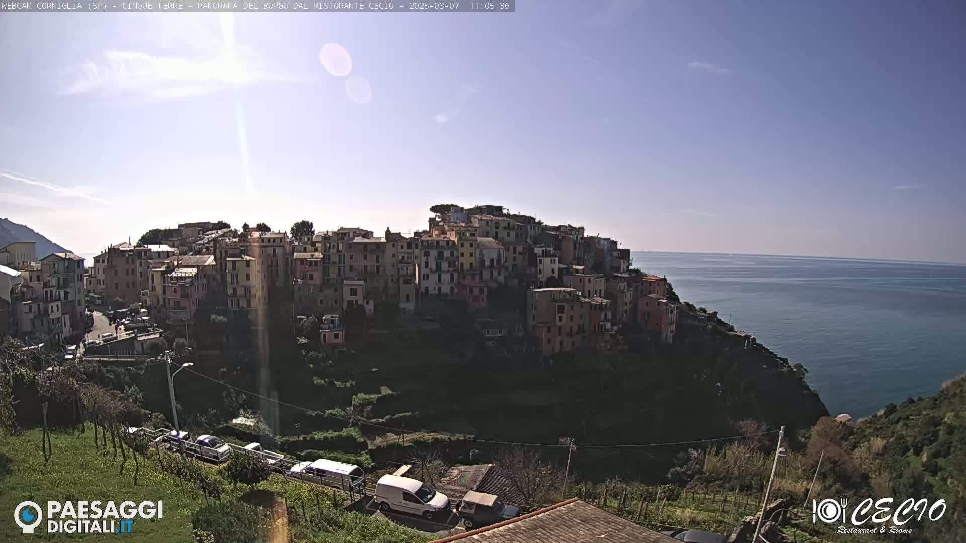 A sunny day reveals a colorful hillside village overlooking a calm blue sea.
