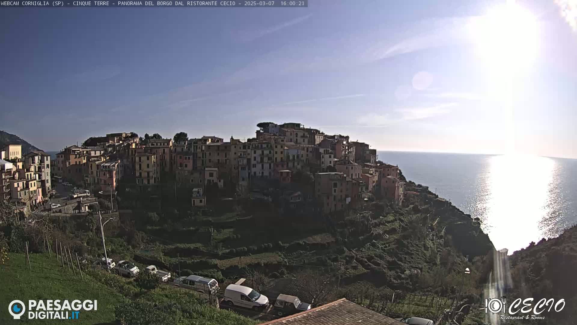 A hillside village of colorful buildings overlooks a calm, sunlit sea.