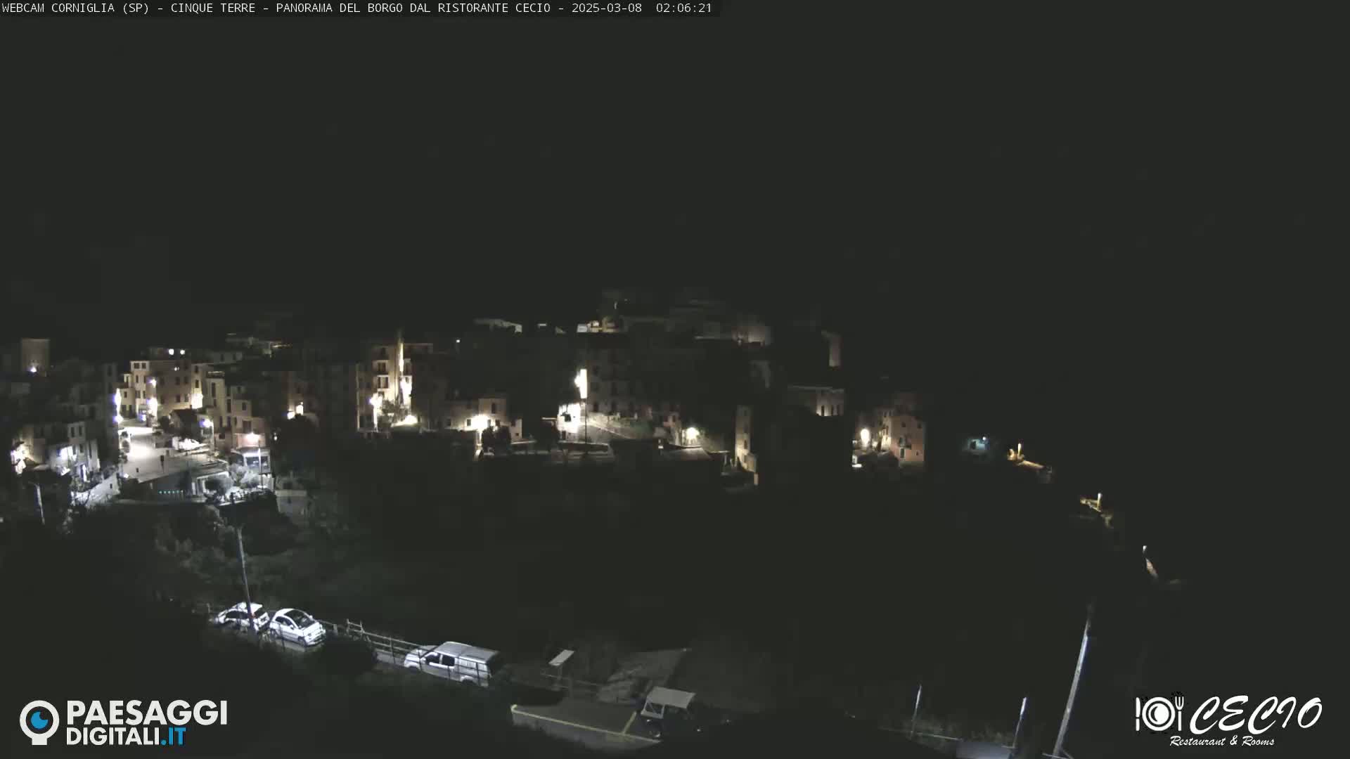 A nighttime, high-angle view shows a small, dimly lit town nestled on a hillside.
