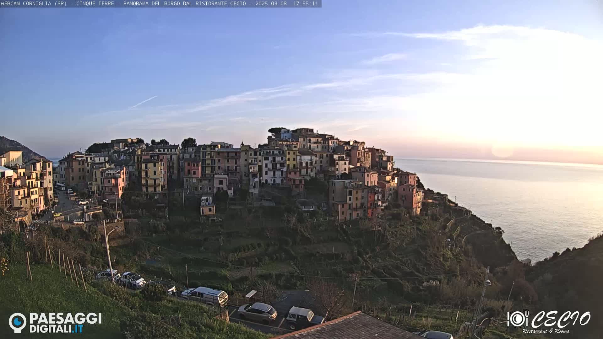 A coastal village of colorful buildings on a hillside overlooking a calm sea at sunset.