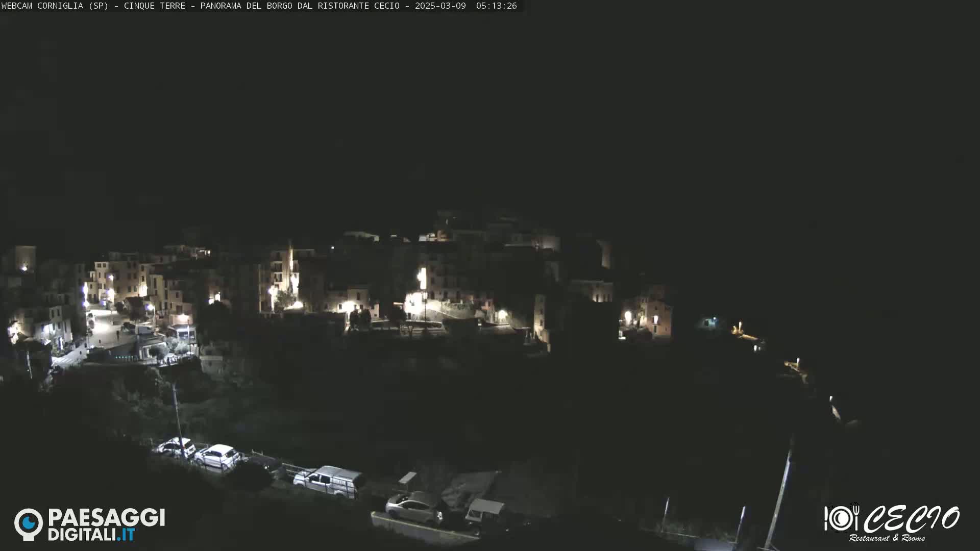 A nighttime, high-angle view of a small, dimly lit town nestled on a hillside.