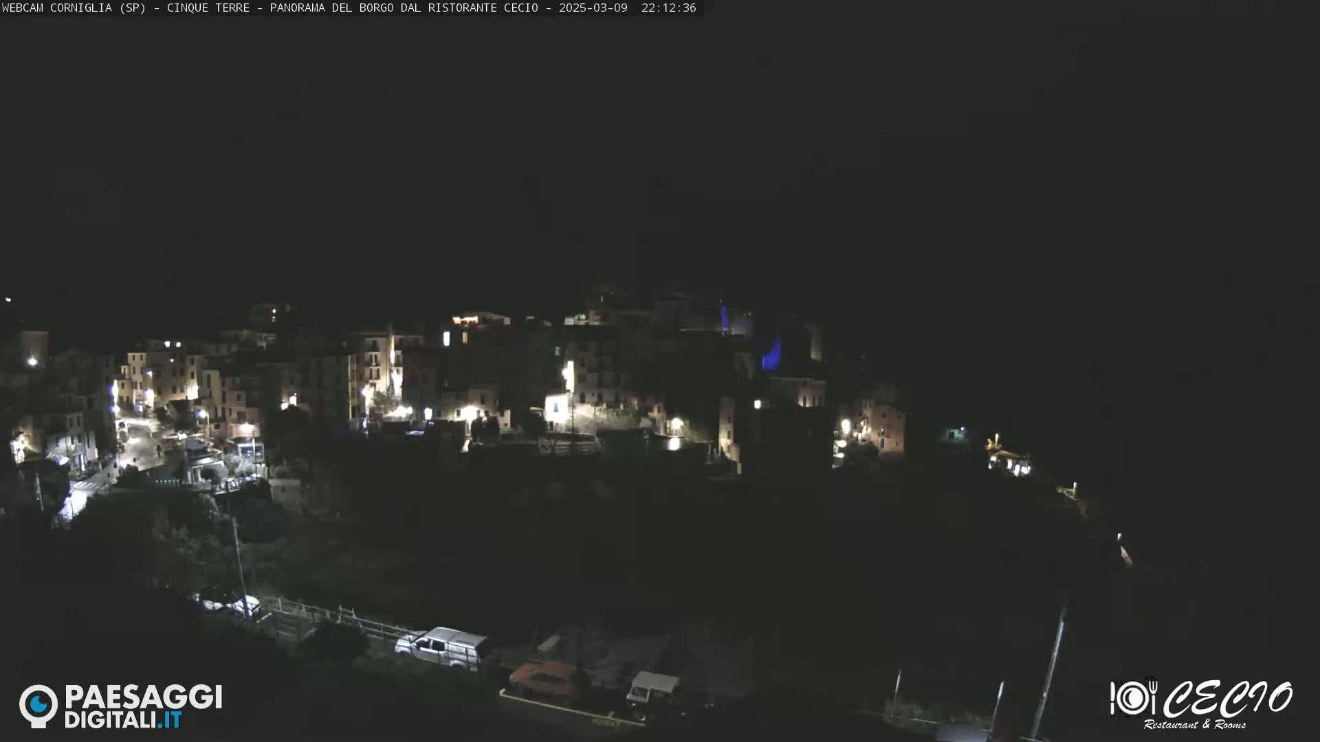 A nighttime, aerial view of a small, illuminated town nestled on a dark hillside.