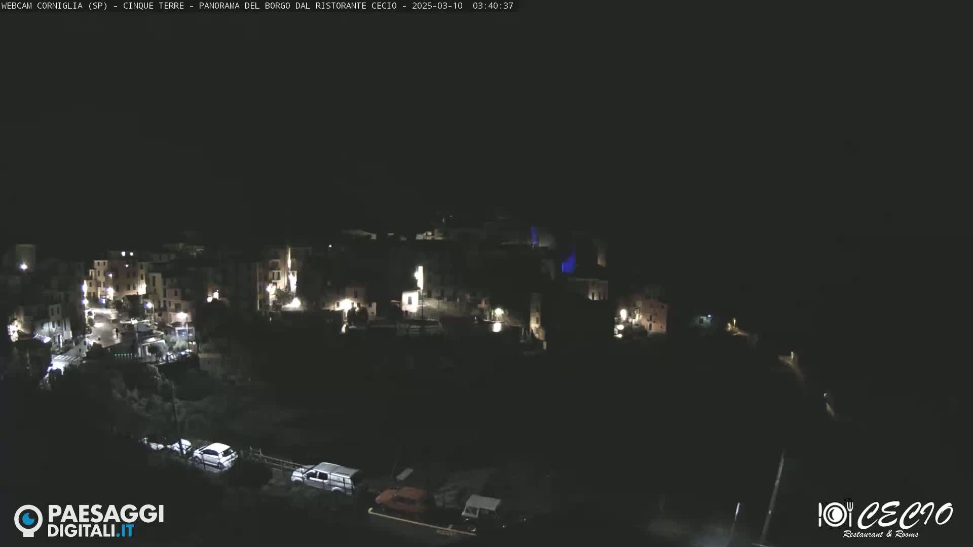 A nighttime, high-angle view of a small, illuminated village nestled on a dark hillside.